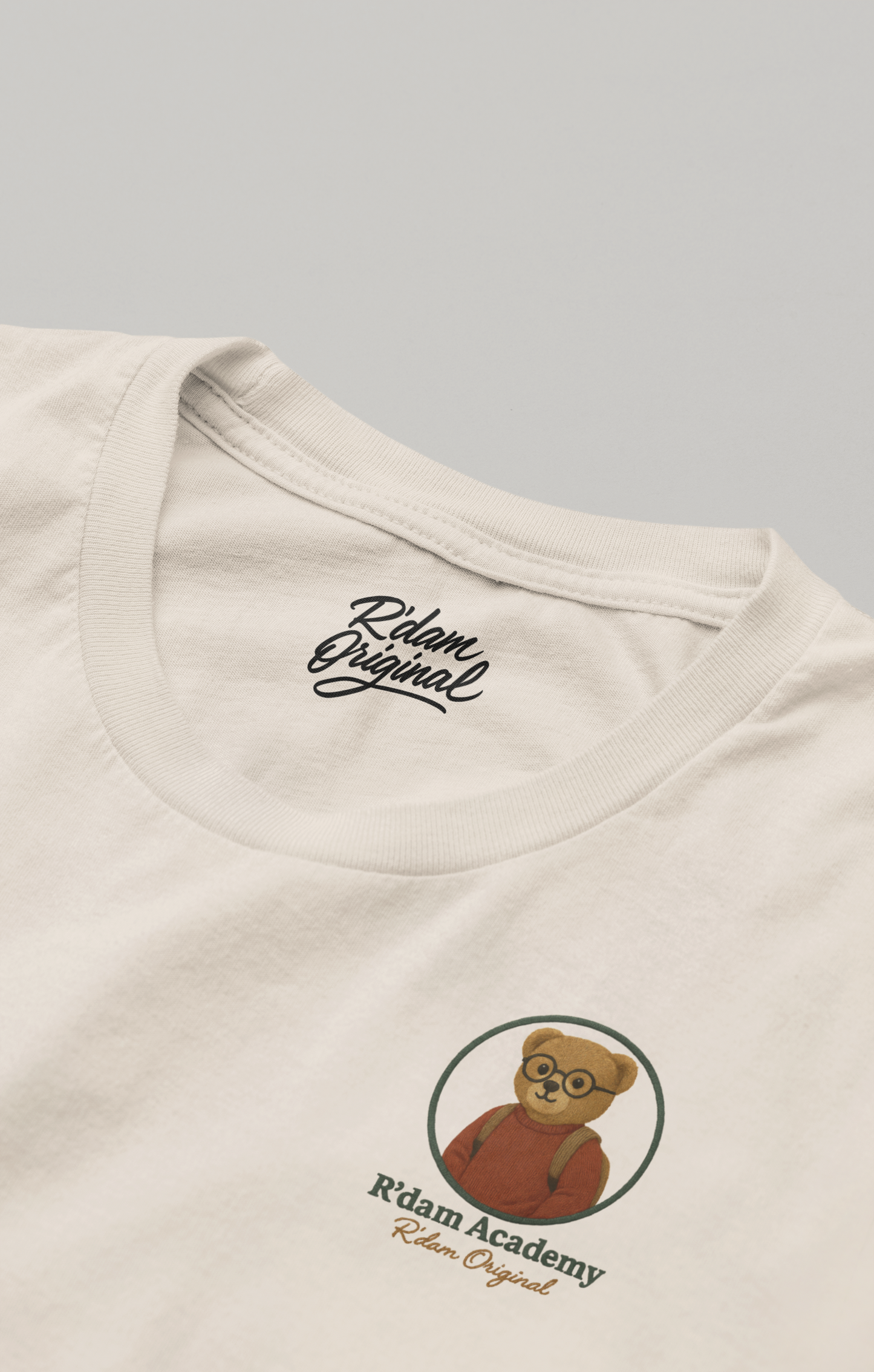"Beige R’dam Academy T-shirt met teddybeer in hoodie, zittend met boeken en koffie" borstlogo